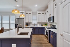 Une cuisine moderne avec des meubles blancs, un îlot central, des appareils en acier inoxydable et des luminaires suspendus.