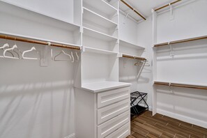 Un armario blanco con estantes, espacio para colgar ropa, suelo de madera y una estructura metálica negra.