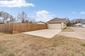 A residential garage with a wooden fence, a concrete driveway, and a house with a gabled roof.
