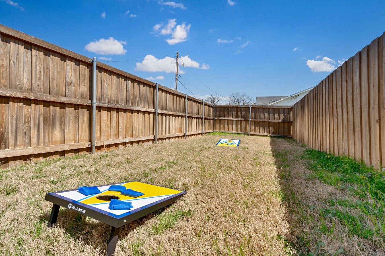 Un jardin avec une clôture en bois, une petite pelouse et une table sur laquelle se trouve un objet bleu et jaune.