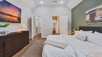 Une chambre moderne avec un grand lit, une commode, un tableau et une vue sur un couloir.