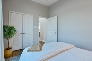 A bedroom with a bed, two white doors, a potted plant, and a woven basket.