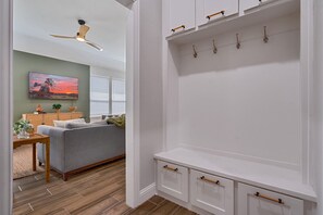Ein Wohnzimmer mit grauem Sofa, Holzschrank mit Haken und Deckenventilator.
