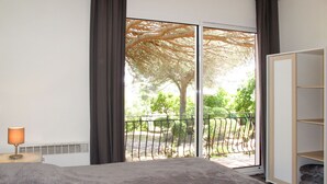 Ein Schlafzimmer mit einem Bett, einem Nachttisch, einer Lampe, einer Schiebetür zu einem Balkon und einem Kleiderschrank.