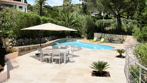 Ein Swimmingpool mit Liegestühlen und einem Tisch, umgeben von Grünpflanzen und einer Steinmauer.
