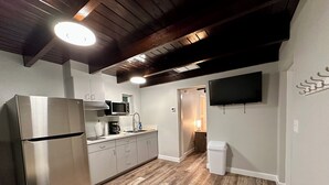 Una cocina moderna con un refrigerador de acero inoxidable, un microondas y una cafetera. El suelo es de madera y hay un bote de basura blanco.