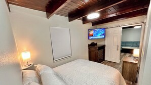 Un dormitorio con cama, lámparas de noche, televisor, cómoda y una puerta que da a otra habitación.
