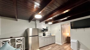 Cocina compacta con refrigerador, microondas y pileta. Tiene techo de madera y un televisor montado en la pared.