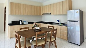A modern kitchen with wooden cabinets, a stainless steel refrigerator, and a dining table with chairs. - Baan First Pool Villa (Koh Samui)