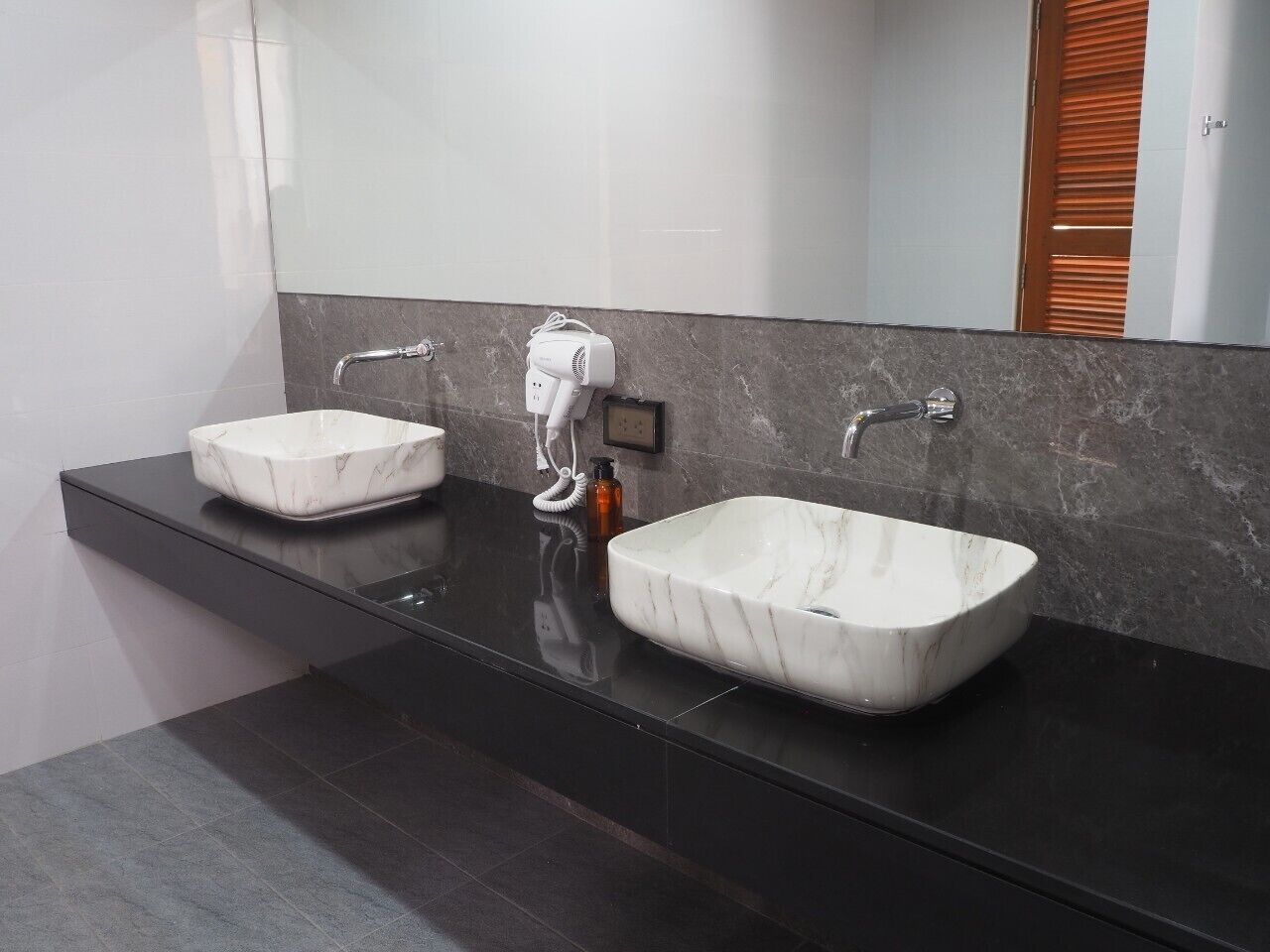 Un baño moderno con dos lavamanos de mármol, un espejo grande y una encimera oscura.