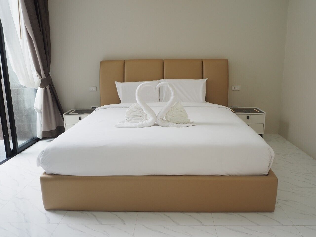 A hotel room with a large bed, two pillows, a nightstand, and a window with curtains.