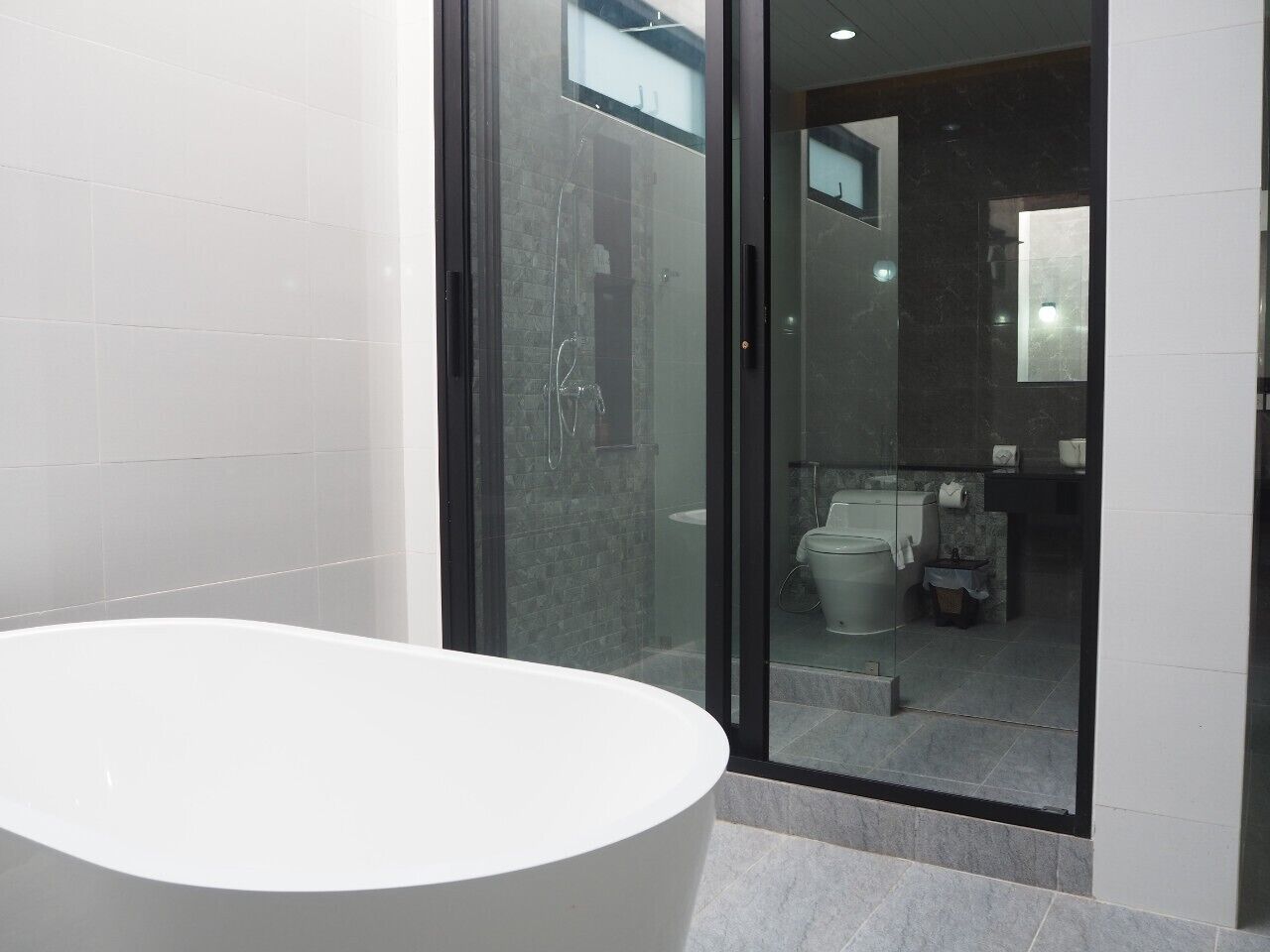 Un baño moderno con una bañera independiente, un box de ducha de cristal y un área visible para el inodoro y el lavamanos.