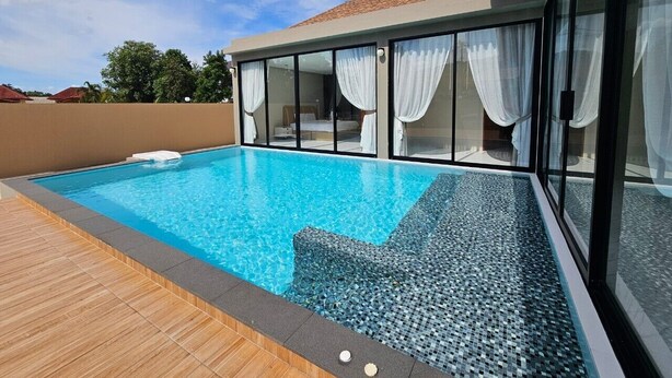 A modern outdoor swimming pool with clear blue water, surrounded by a wooden deck and glass walls. - Baan First Pool Villa (Koh Samui)
