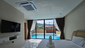 A hotel room with a large bed, a flat-screen TV mounted on the wall, and a view of a swimming pool through large windows. - Baan First Pool Villa (Koh Samui)