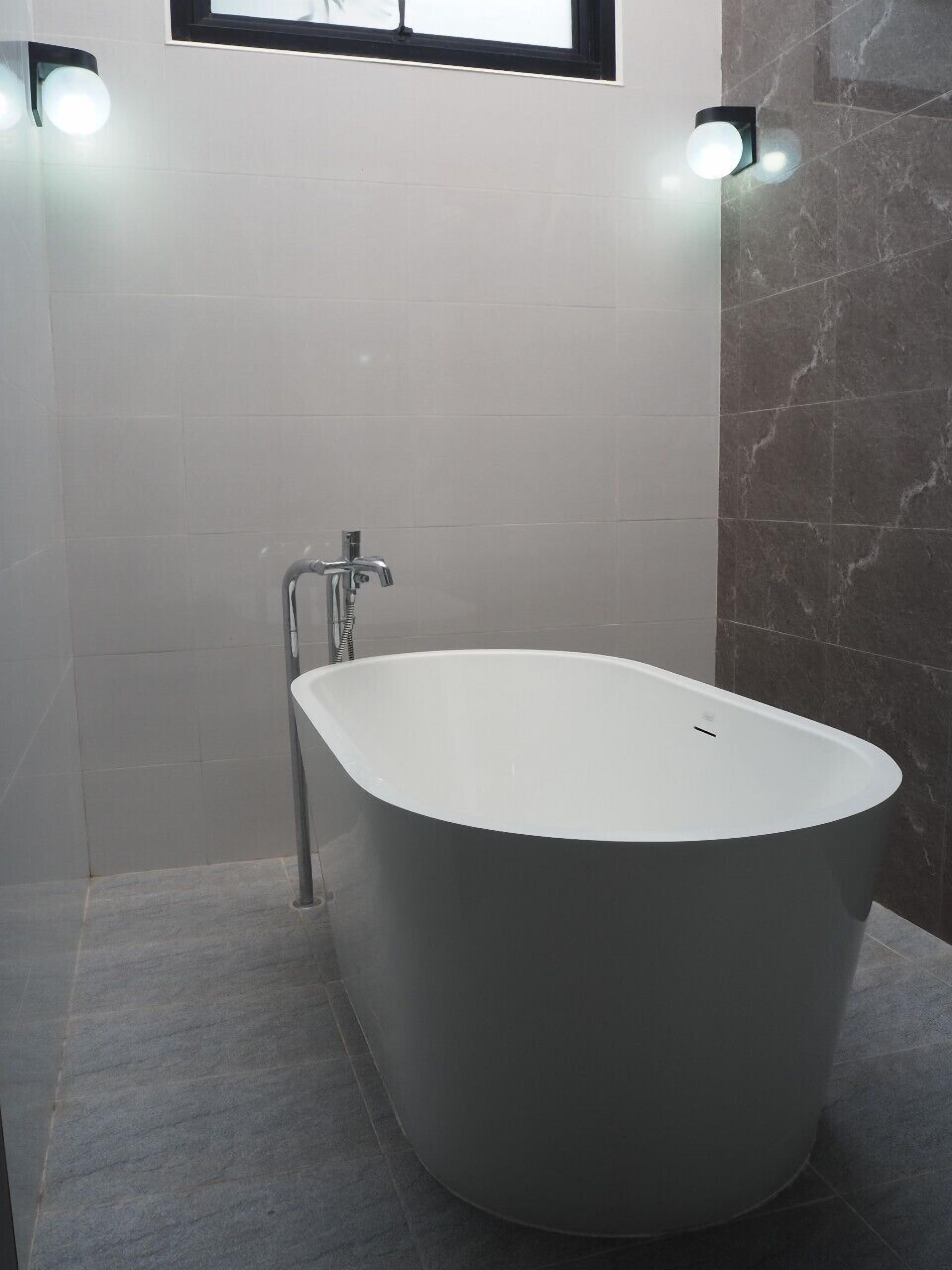 Un baño moderno con una bañera independiente, un ventanal y dos luces fijadas a la pared.