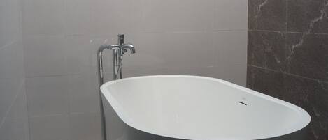 Un baño moderno con una bañera independiente, un ventanal y dos luces fijadas a la pared.