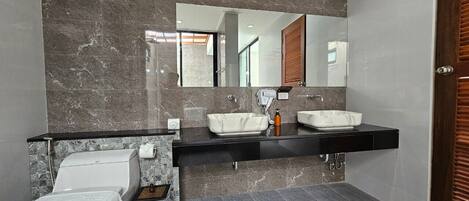 A modern bathroom with a marble wall, a black countertop, a white sink, and a toilet.