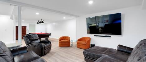 Una sala de estar moderna con sofás de cuero, mesa de billar y televisor de pantalla plana montado en la pared.
