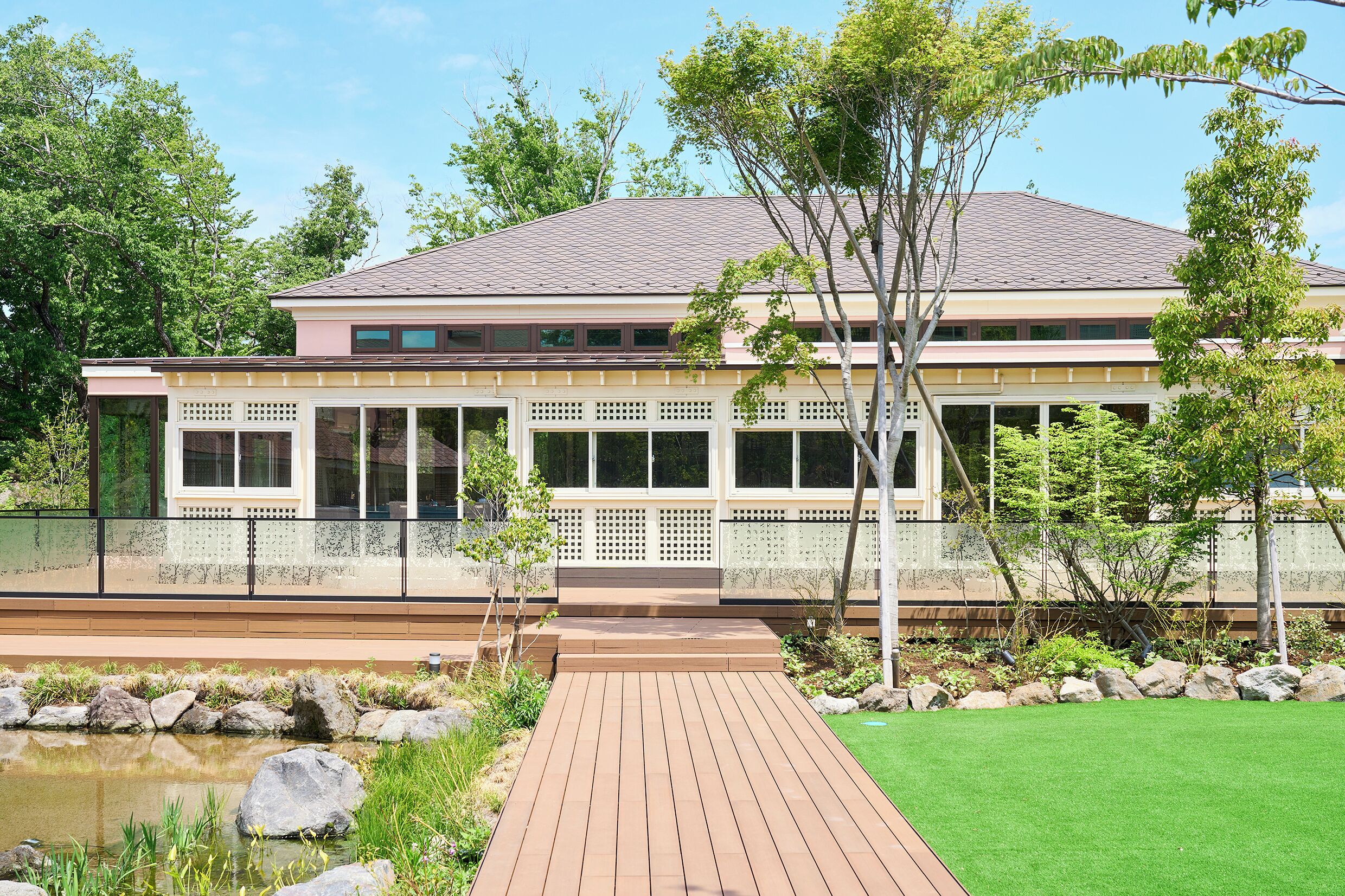 A modern house with a large deck, a pond, and a well-maintained lawn.