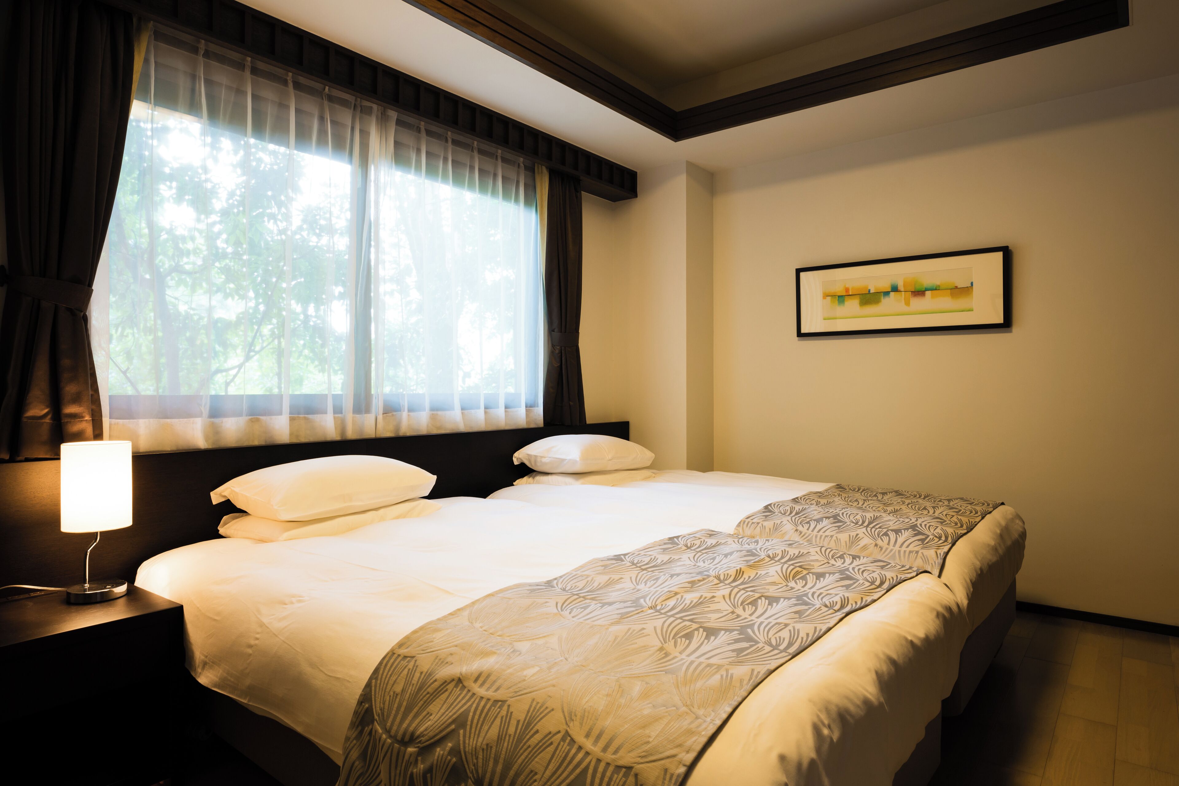 A hotel room with a bed, a nightstand, a lamp, a window with curtains, and a framed picture on the wall.