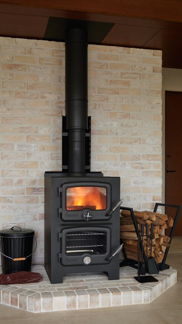 A wood-burning stove with a glass front, a chimney, and a log storage area. - ADVENTURES ISLAND KOYARUZAWA LODGE (Yachimata)