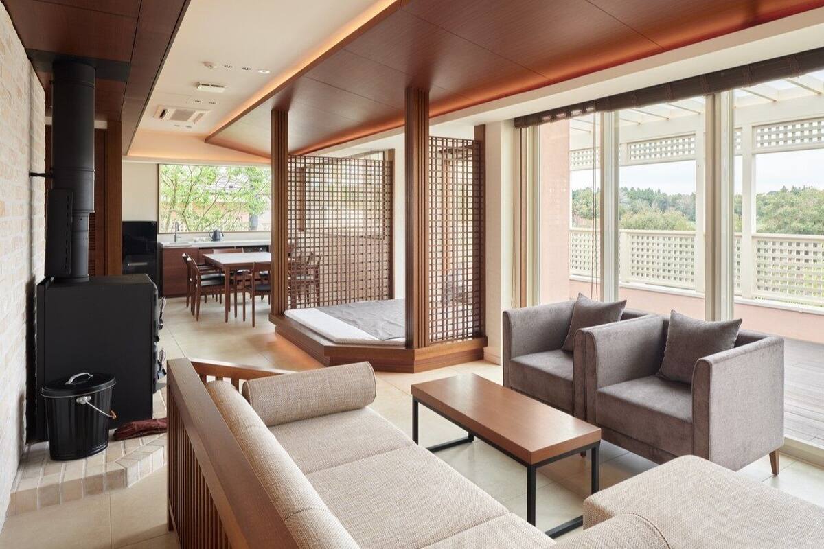Ein modernes Wohnzimmer mit einer Couch, Sesseln und einem Esstisch. Ein großes Fenster bietet Blick auf Grünflächen.