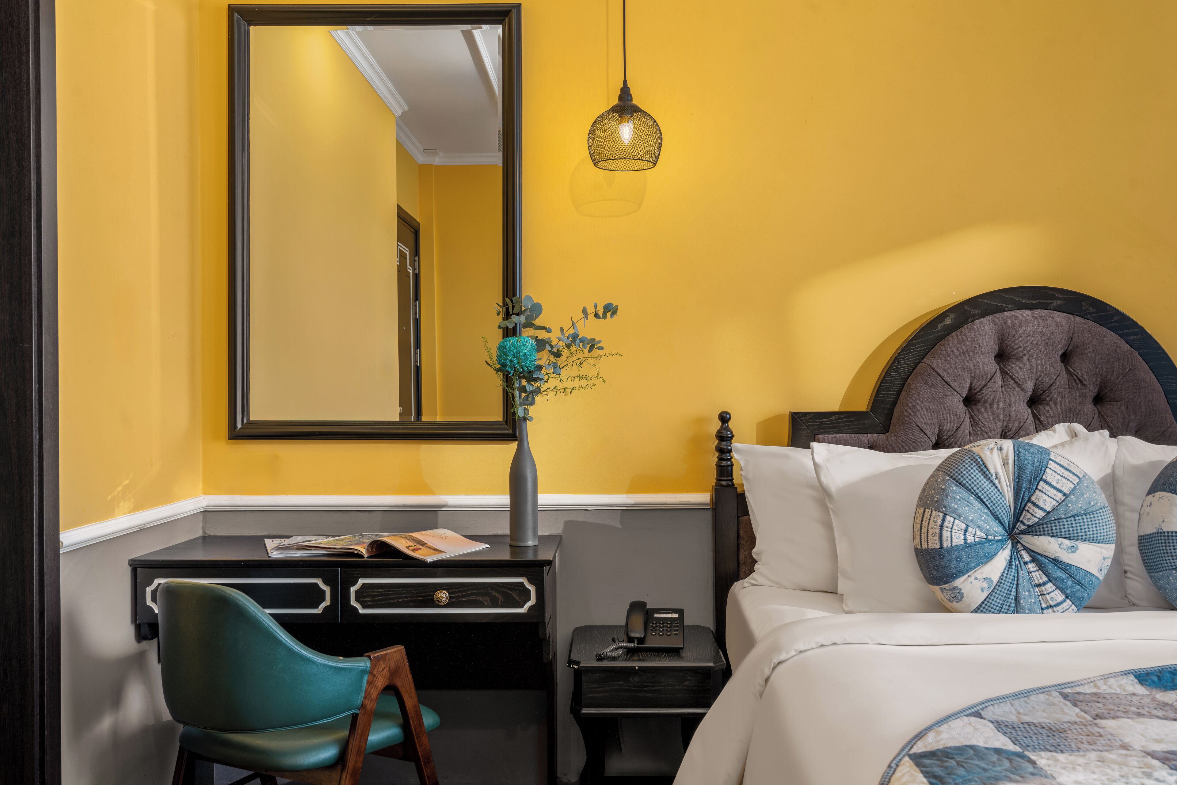 A hotel room with a bed, a desk, a chair, a nightstand, a lamp, and a mirror.