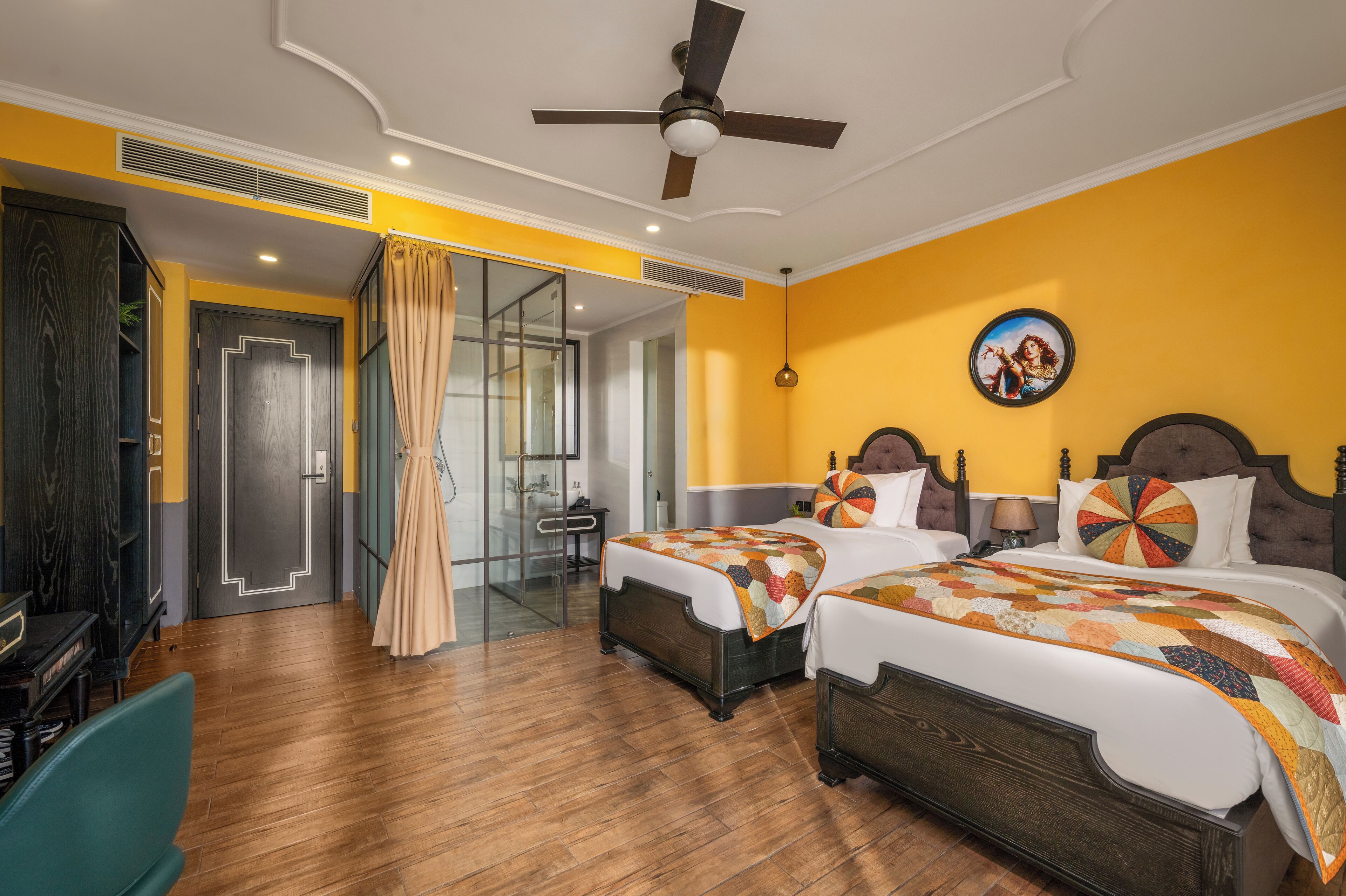 A hotel room with two beds, a ceiling fan, a large window with curtains, and a television.