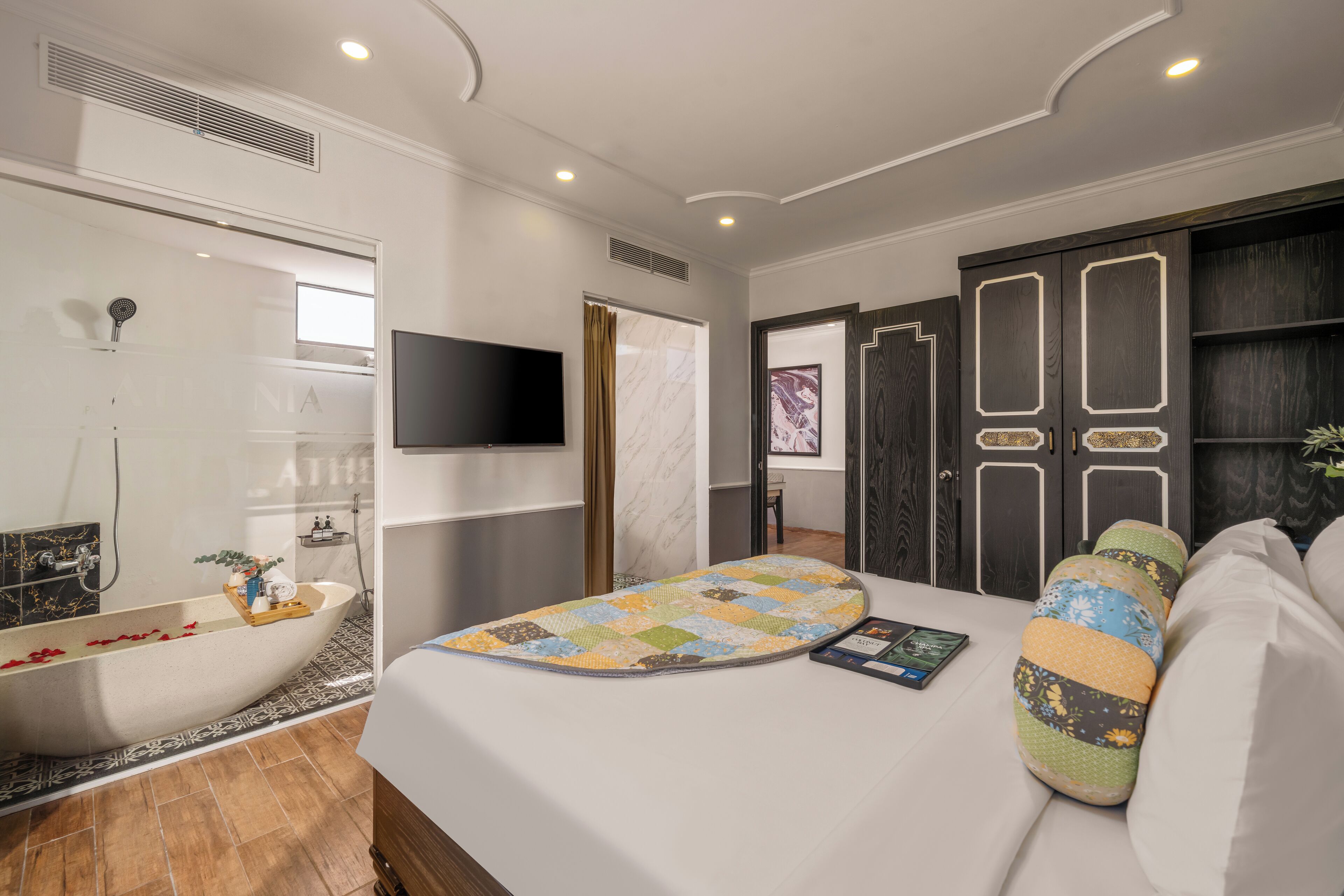 A modern bedroom with a large bed, a built-in bathtub, a television, and a dark wooden wardrobe.