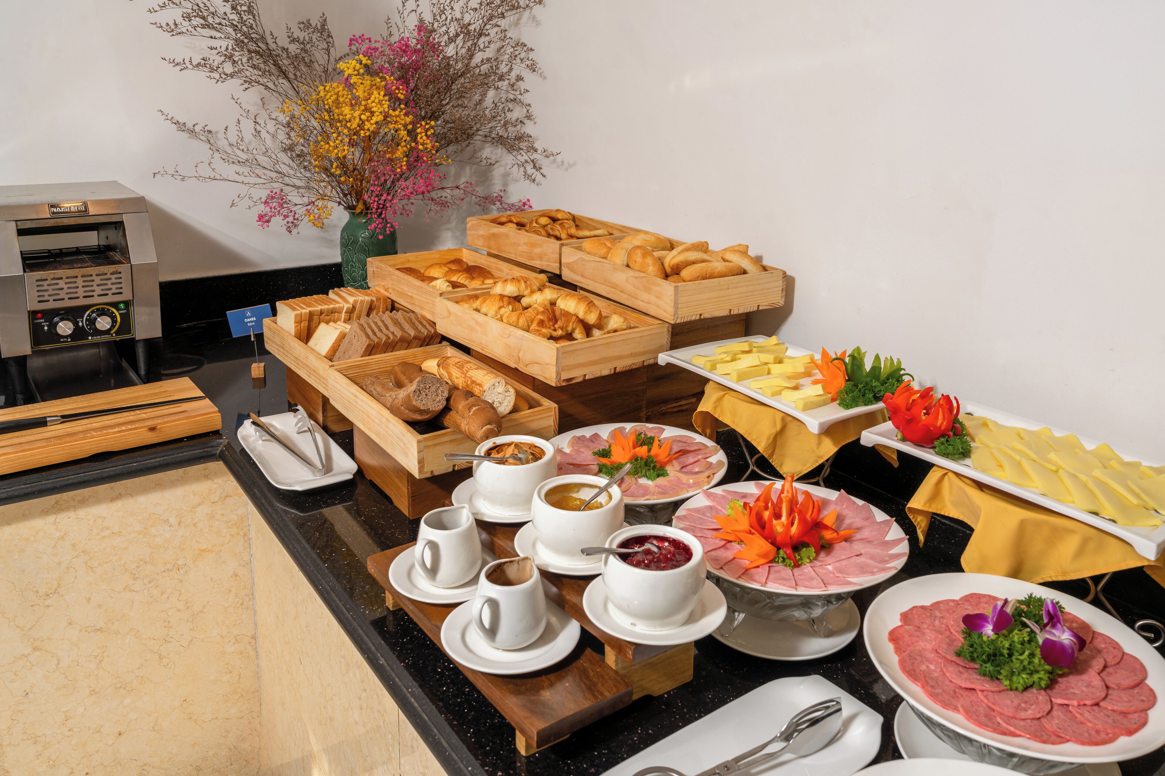 Buffet com diversos alimentos, incluindo pão, doces e carnes, dispostos em um balcão.