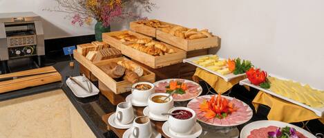 Buffet com diversos alimentos, incluindo pão, doces e carnes, dispostos em um balcão.