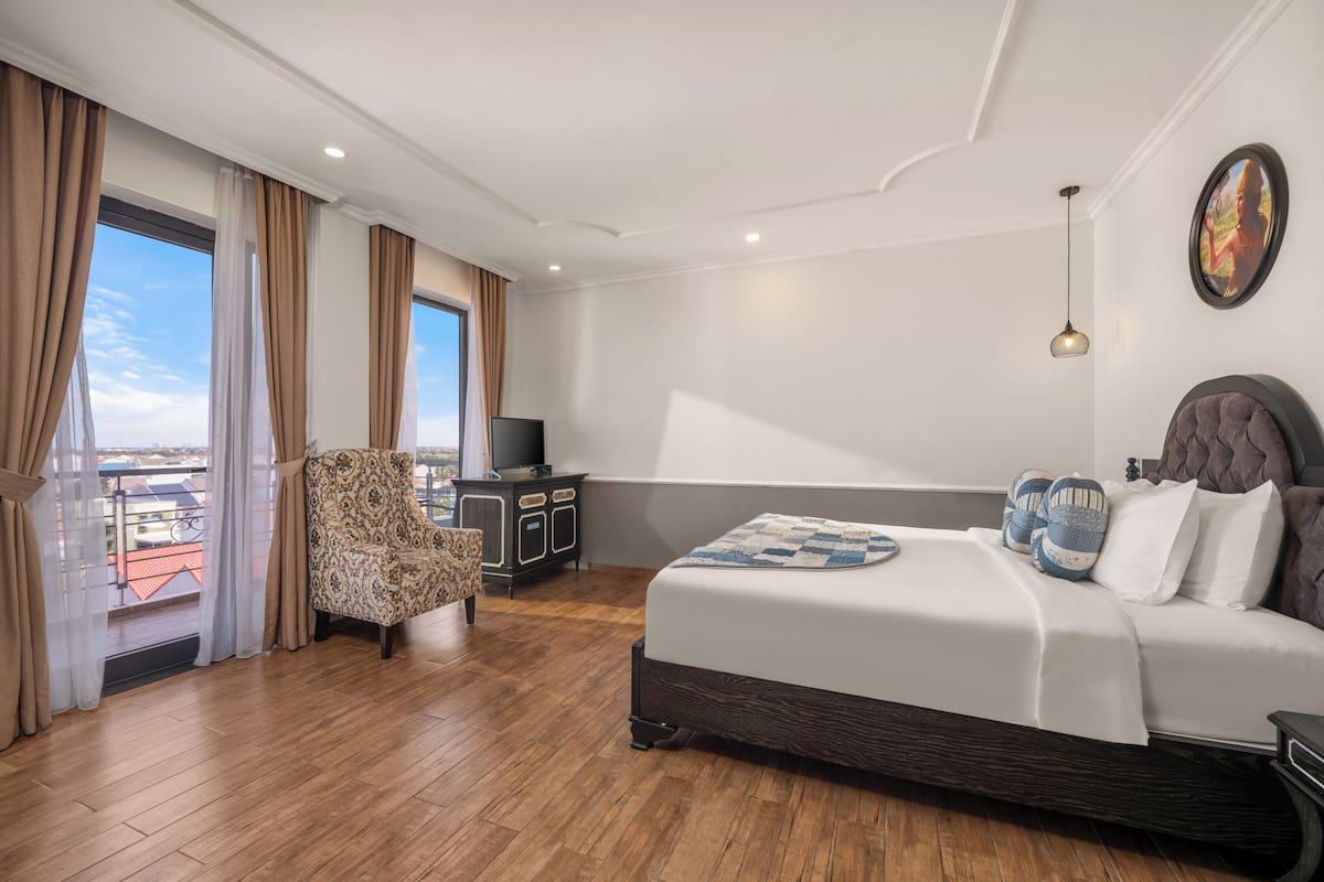 A hotel room with a large bed, a chair, a desk with a TV, and a view of the city.