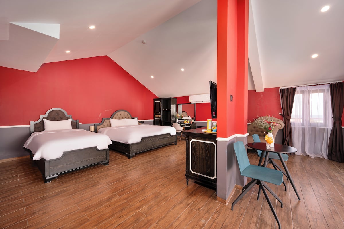 A hotel room with two beds, a dining area with a table and chairs, and a red accent wall.