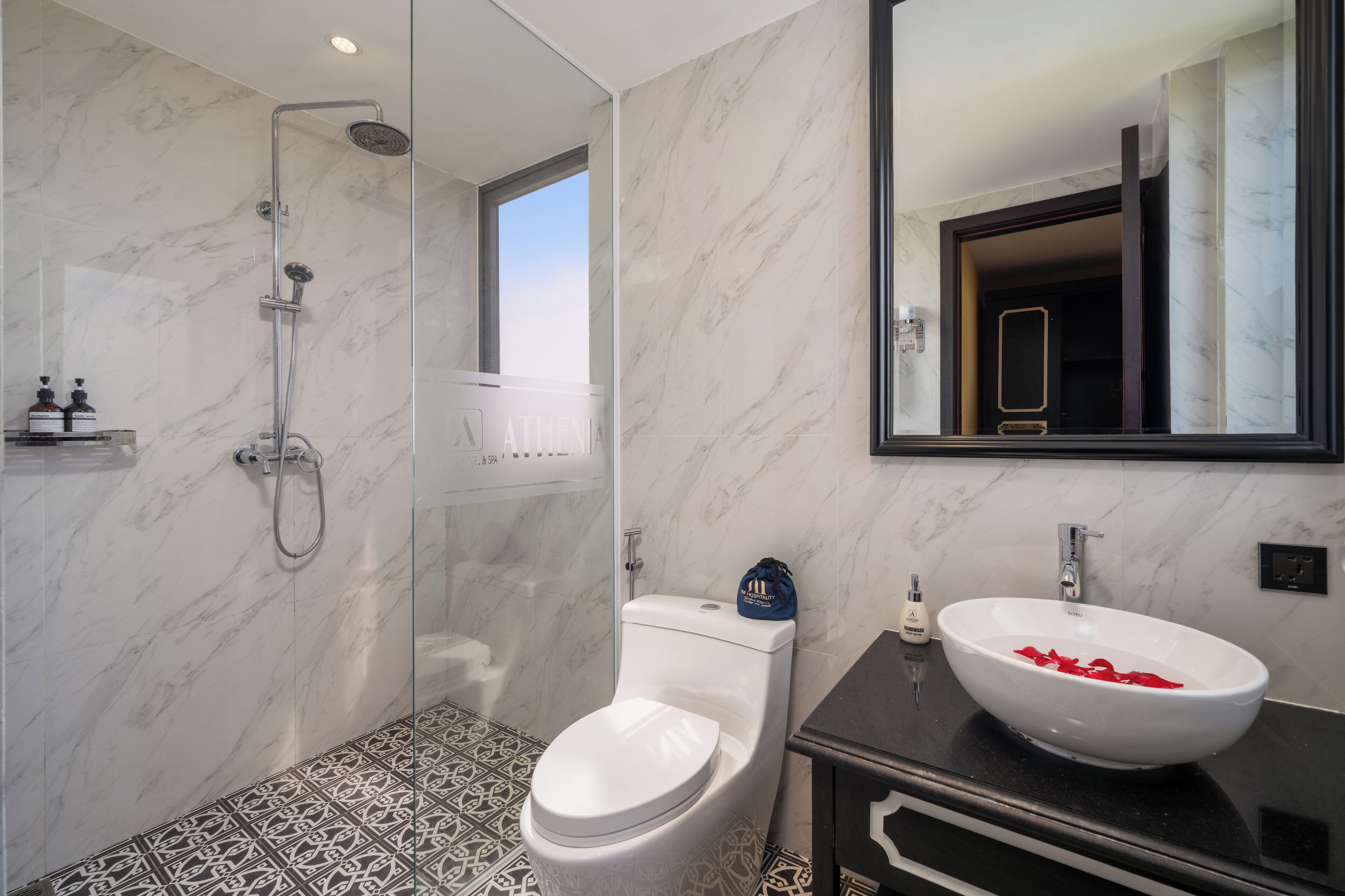 A modern bathroom with a glass-enclosed shower, a white toilet, and a large white sink with red flowers.