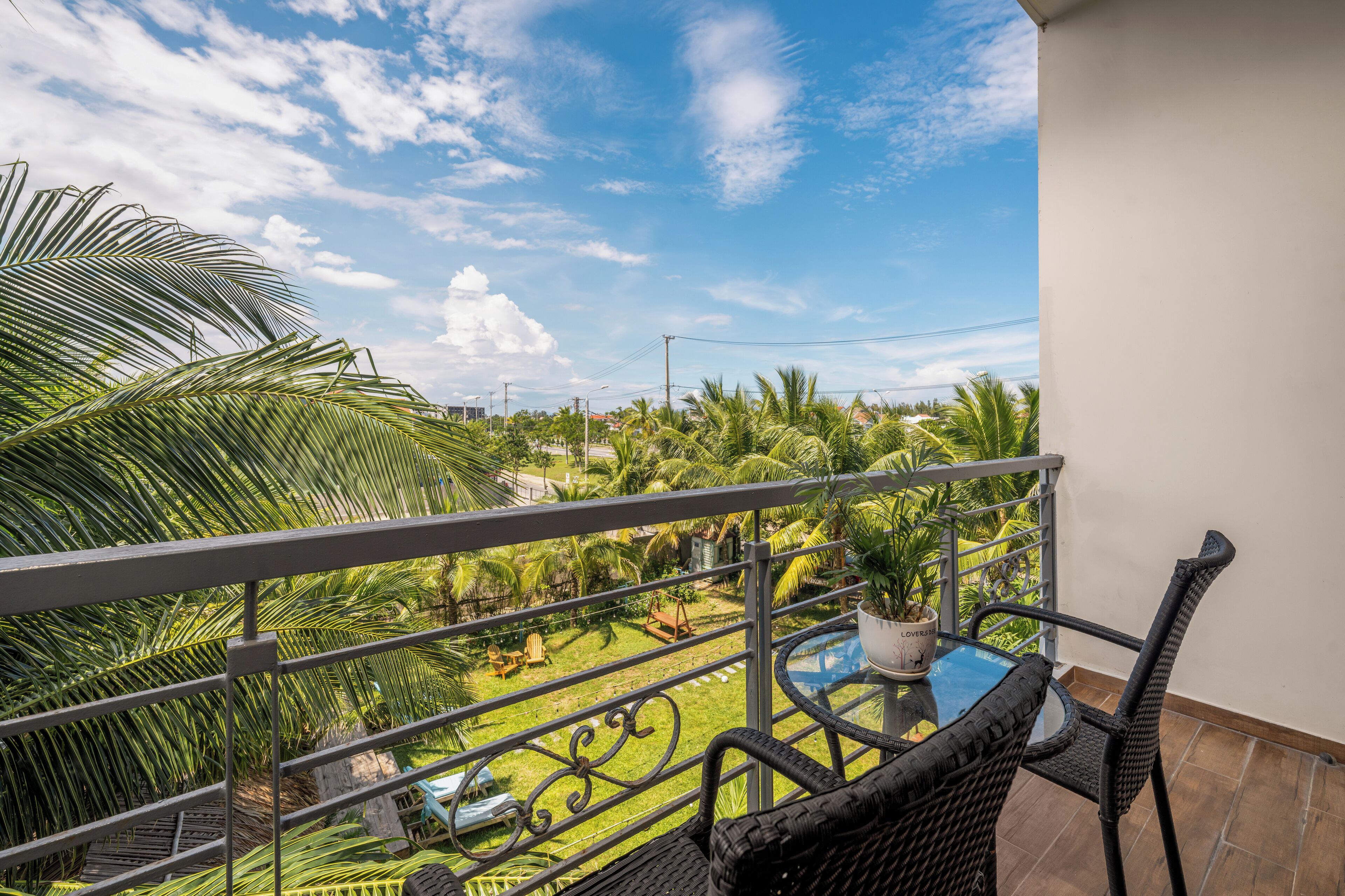 A balcony with a view of a garden, a table, and chairs.