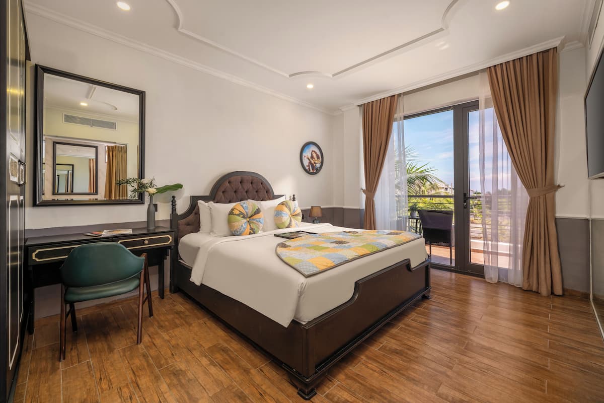 A hotel room with a large bed, a desk, a chair, a mirror, and a view of the outdoors.
