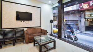 Een moderne lobby met een flatscreen televisie aan de wand, een bruine bank en een salontafel met een glazen blad.