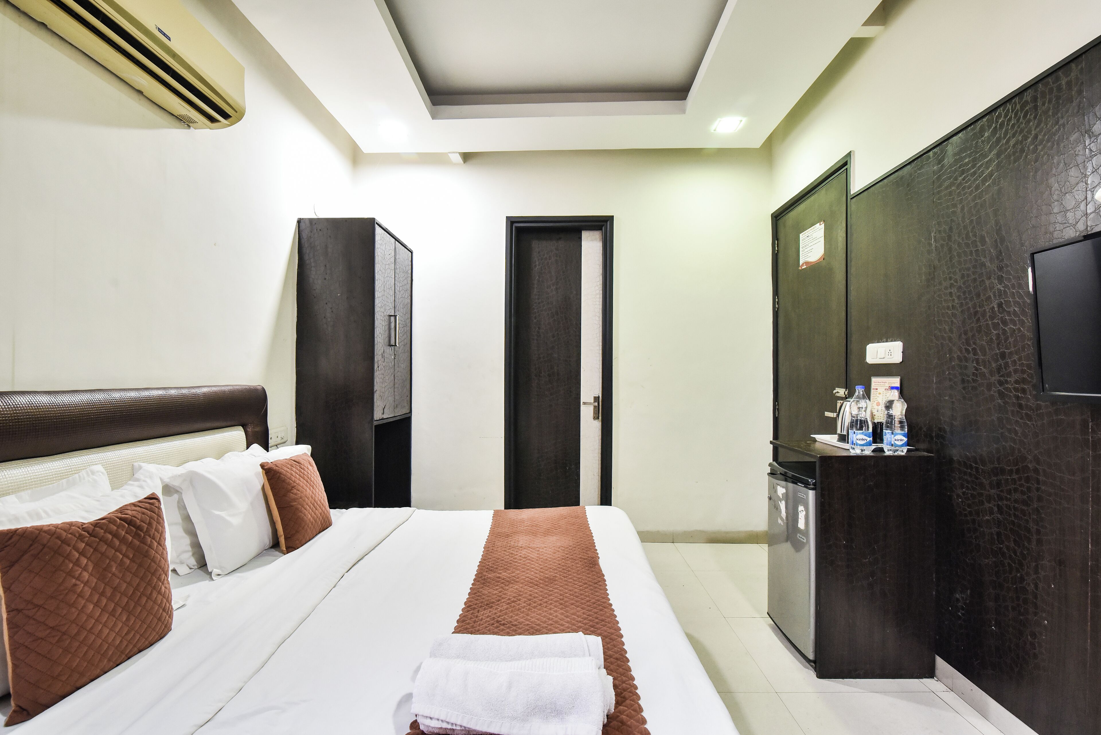 A hotel room with a bed, a wardrobe, a minibar, and an air conditioning unit.