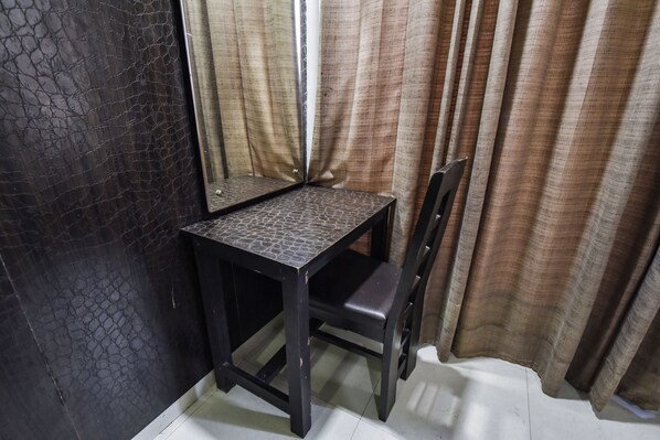 A corner room with a dark textured wall, a small table, a chair, and a curtain. - hotel akaal heights (Amritsar)