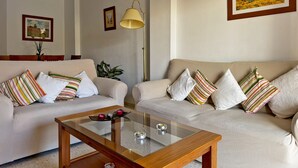 A living room with two sofas, a glass coffee table, and a lamp. There are framed pictures on the walls.