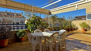 An outdoor patio with a table and chairs, surrounded by potted plants and a view of buildings in the background.