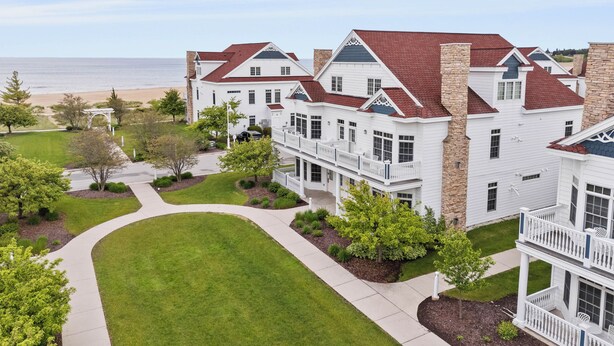 A large, multi-story white building with red roofs, a well-maintained lawn, and a view of the beach. - Breezy Beach | Villa 75 Steps from Lake Michigan (Sheboygan)
