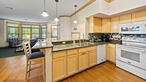 A kitchen with wooden cabinets, a built-in oven, and a large island with bar stools. - Breezy Beach | Villa 75 Steps from Lake Michigan (Sheboygan)