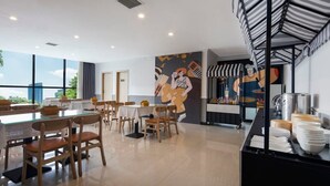 Een moderne eetruimte met glazen tafels en houten stoelen, een muurschildering op de wand en een buffet met borden en kommen.