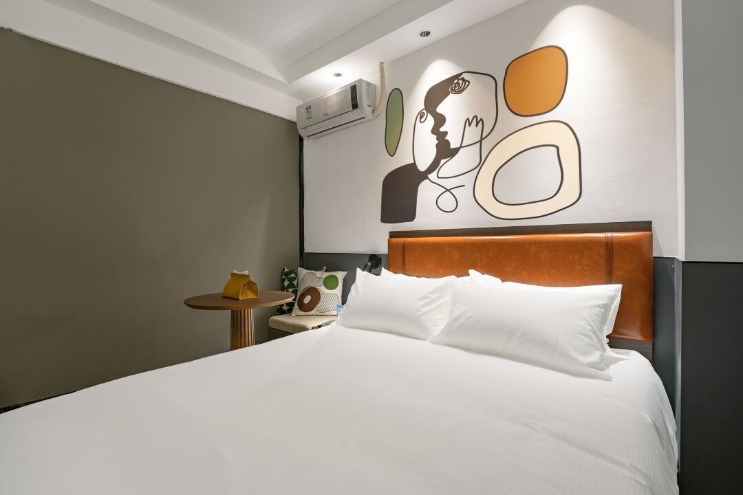 Ein Hotelzimmer mit einem großen Bett, einem runden Nachttisch mit Lampe und einem Wandbild.