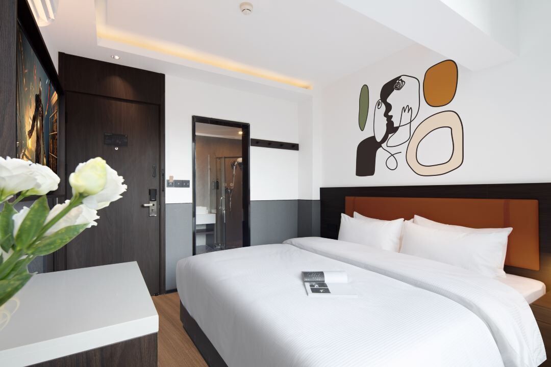 A modern hotel room with a large bed, a bedside table, and a wall art piece.