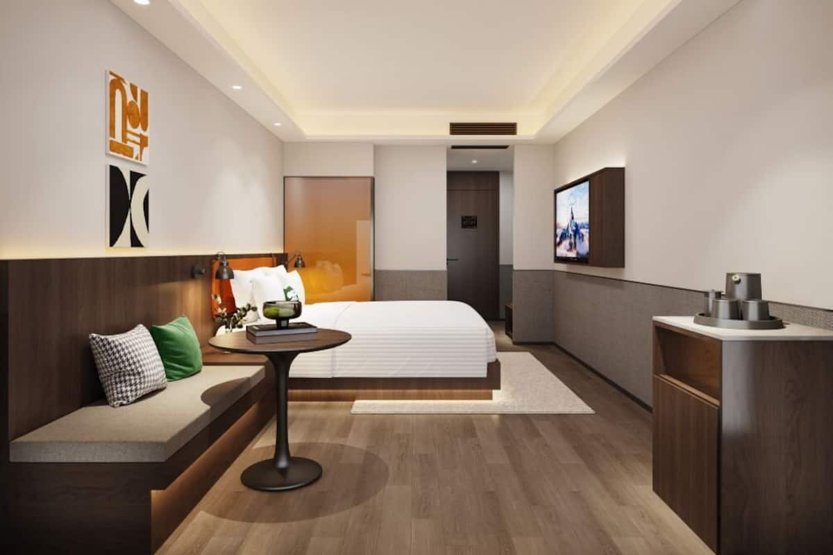Une chambre d’hôtel moderne équipée d’un lit, d’un coin salon, d’une petite table, d’une télévision et d’un mini-bar.