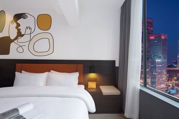 A hotel room with a large bed, a nightstand with a lamp, a view of a cityscape through a window, and a wall art piece above the bed. - Mcsrh Hotel -Shenzhen Bao'an  (Shenzhen)