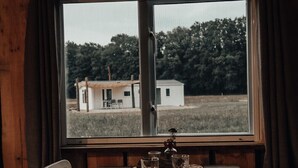 Ein Holzespeisetisch ist gedeckt mit Tellern und Gläsern, eine Vase mit Blumen, und im Fenster ist ein Haus zu sehen.