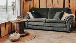 Una habitación acogedora con un sofá gris, una mesa redonda de madera y una cesta de mimbre.